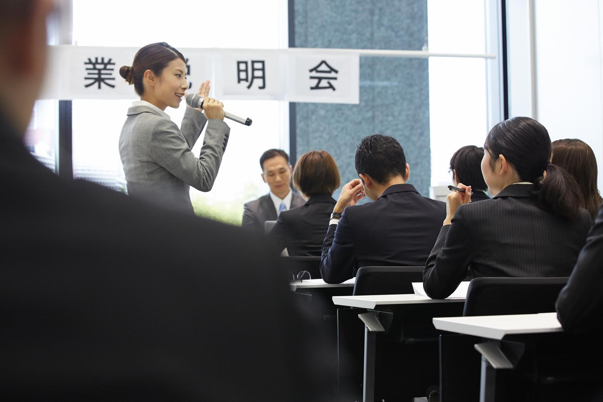 企業説明会でプレゼンする担当者とスーツ姿の人々