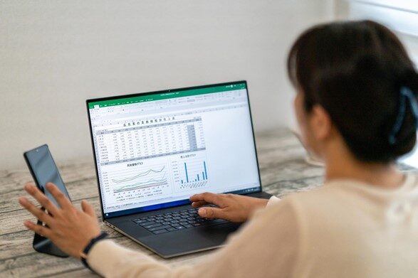 PCに表示されたデータを確認しながらスマホを操作している人