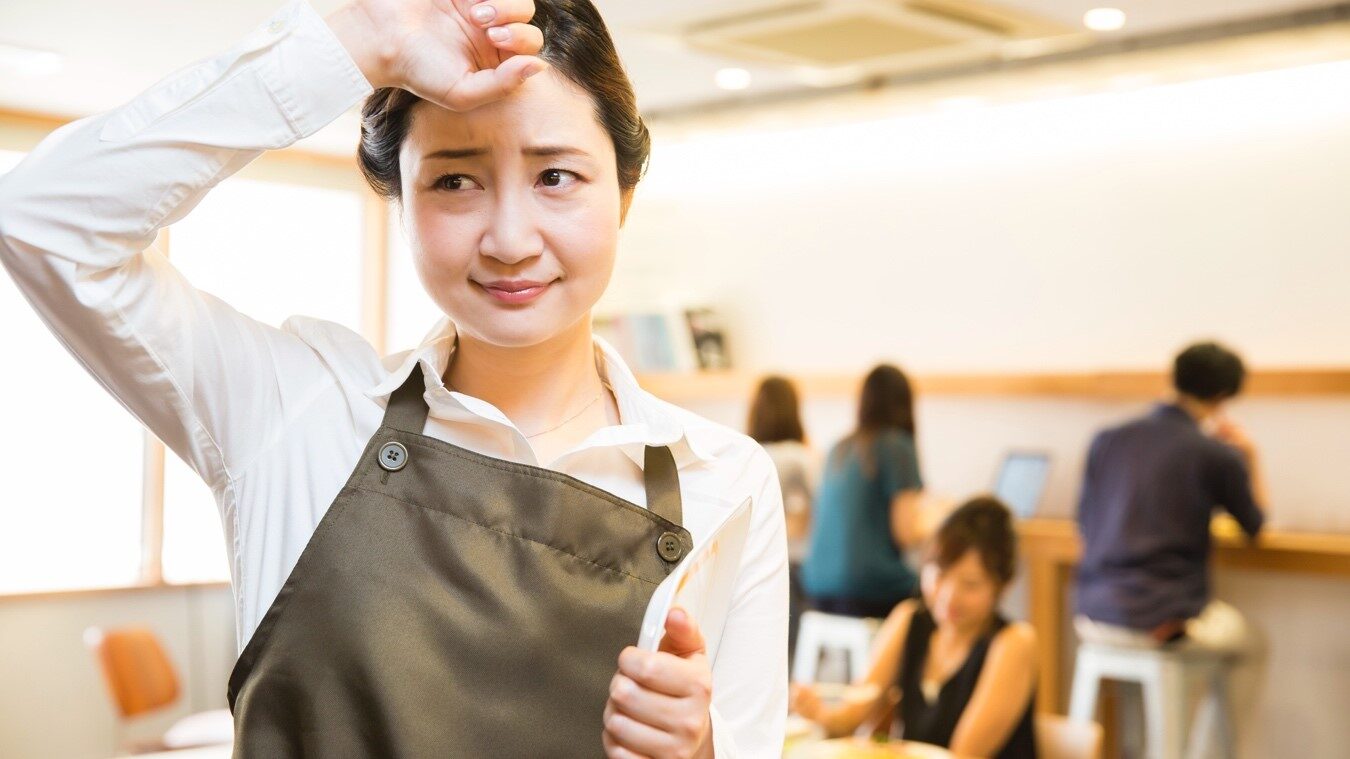 額の汗を拭くエプロン姿の女性店員