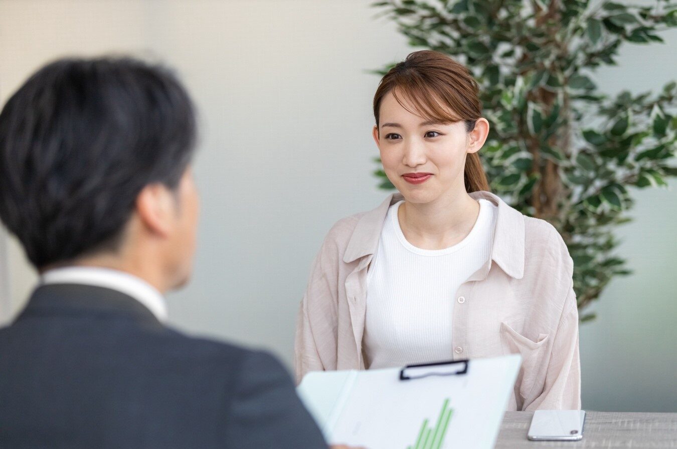 笑顔の女性と、書類を持って正面に座る男性の後ろ姿