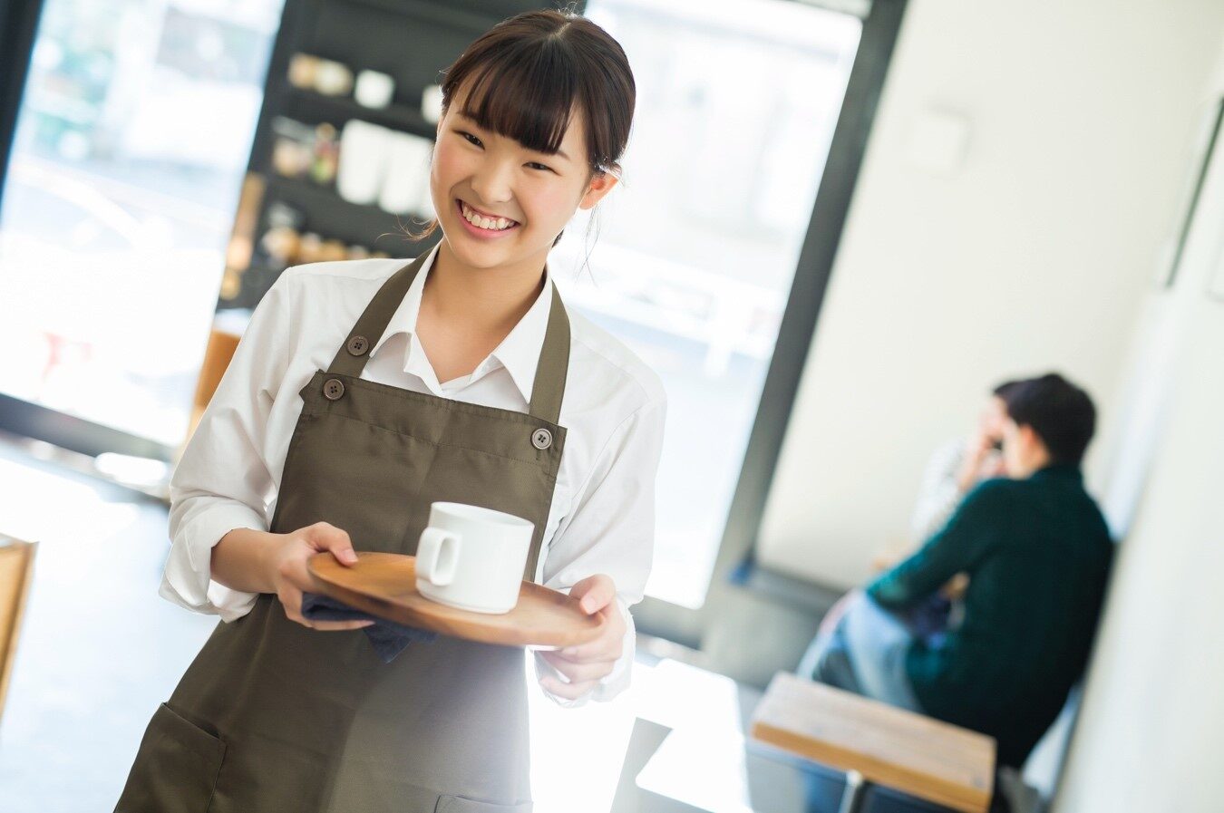 トレイに白いコーヒーカップを乗せた女性店員