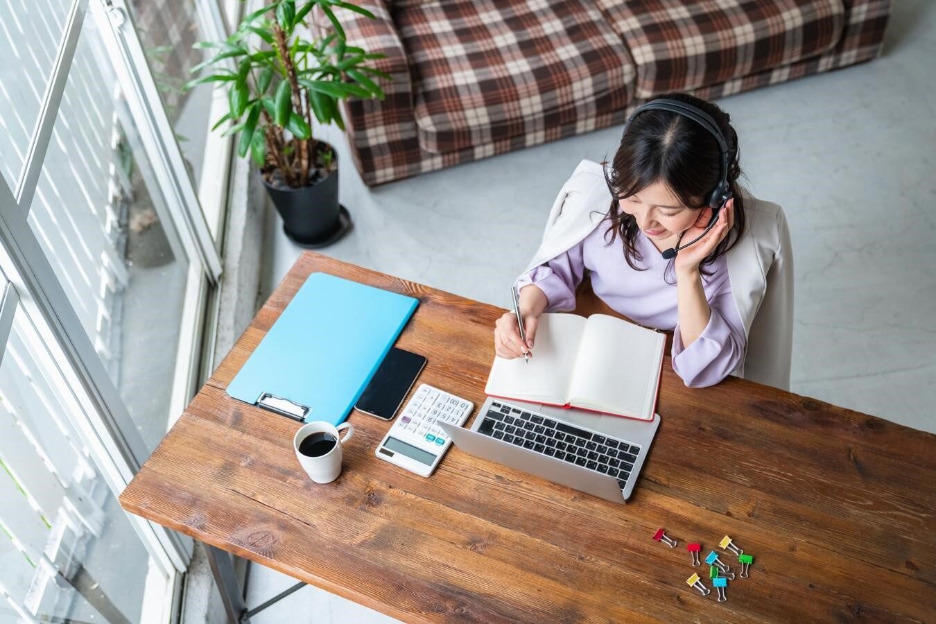 筆記用具を手にヘッドセットを装着してPCに向かう女性