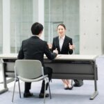 スマホを片手にひとつのスマホを覗き込んでいる4人のビジネスパーソン