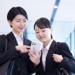 ひとつのスマホを覗き込むスーツ姿の2人の女性