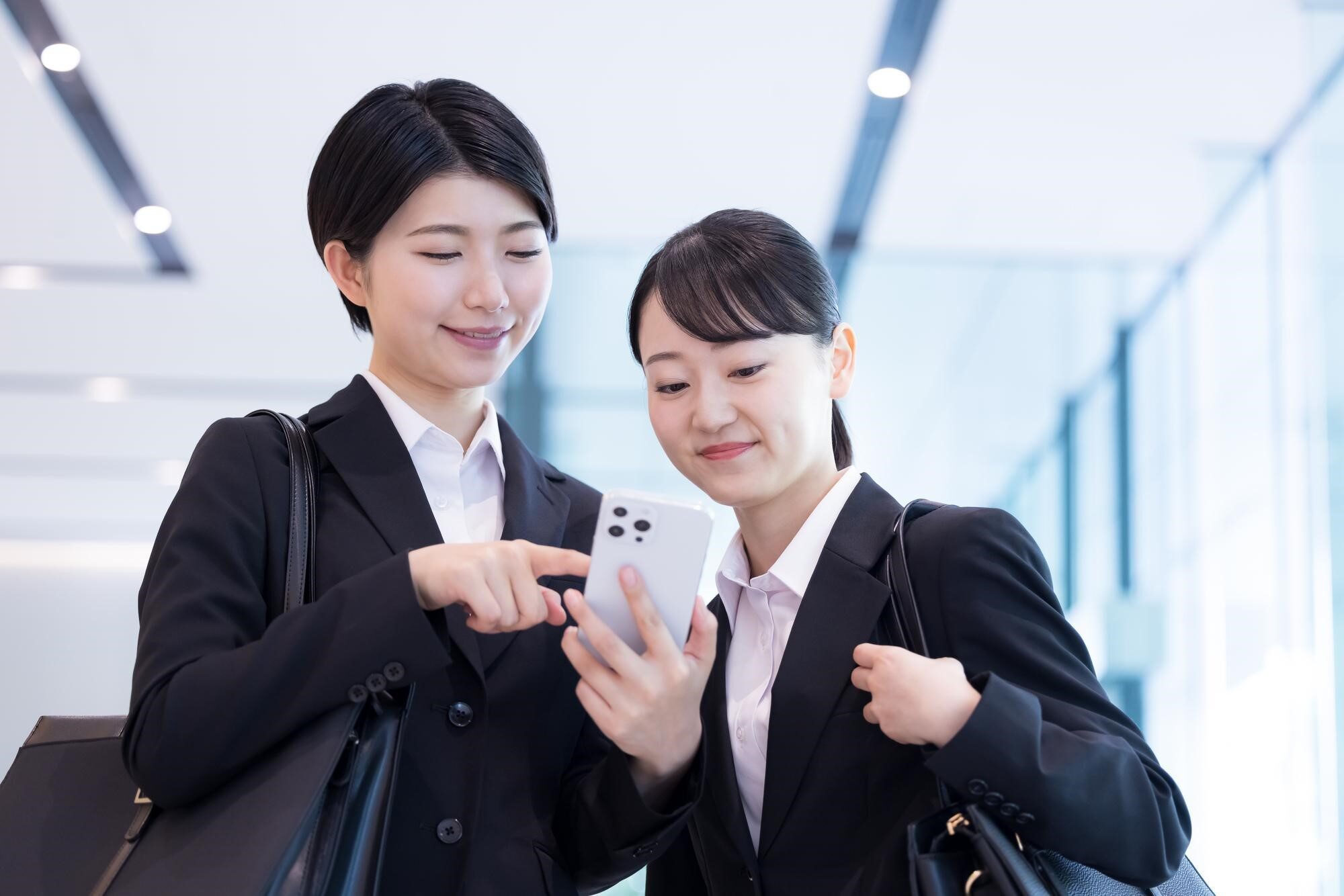 ひとつのスマホを覗き込むスーツ姿の2人の女性