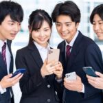 スマホを片手にひとつのスマホを覗き込んでいる4人のビジネスパーソン