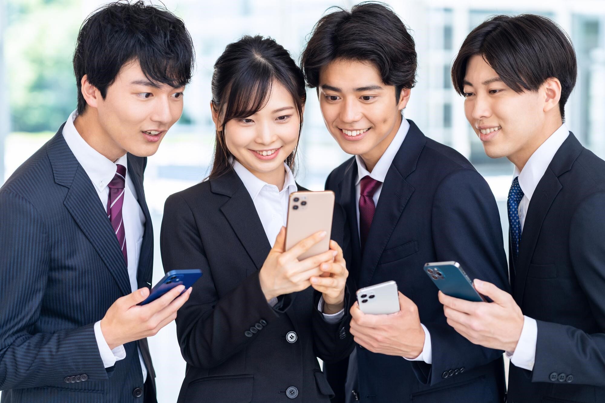 スマホを片手にひとつのスマホを覗き込んでいる4人のビジネスパーソン